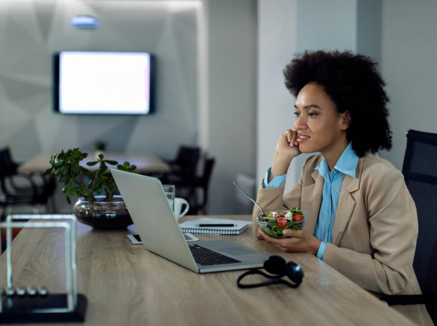 Mulher come salada em frente ao computador durante o trabalho