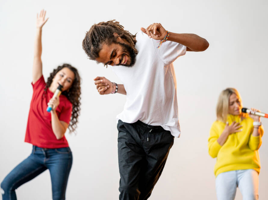 Homem dança enquanto duas mulheres cantam ao fundo.