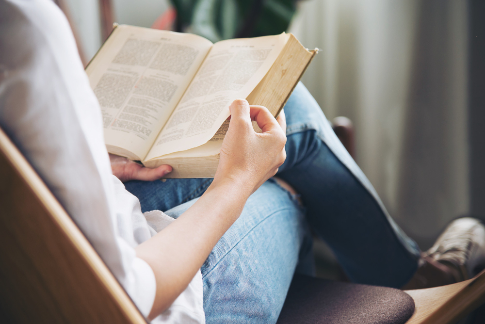 Imagem mostra mulher sentada segurando um livro aberto sobre o colo